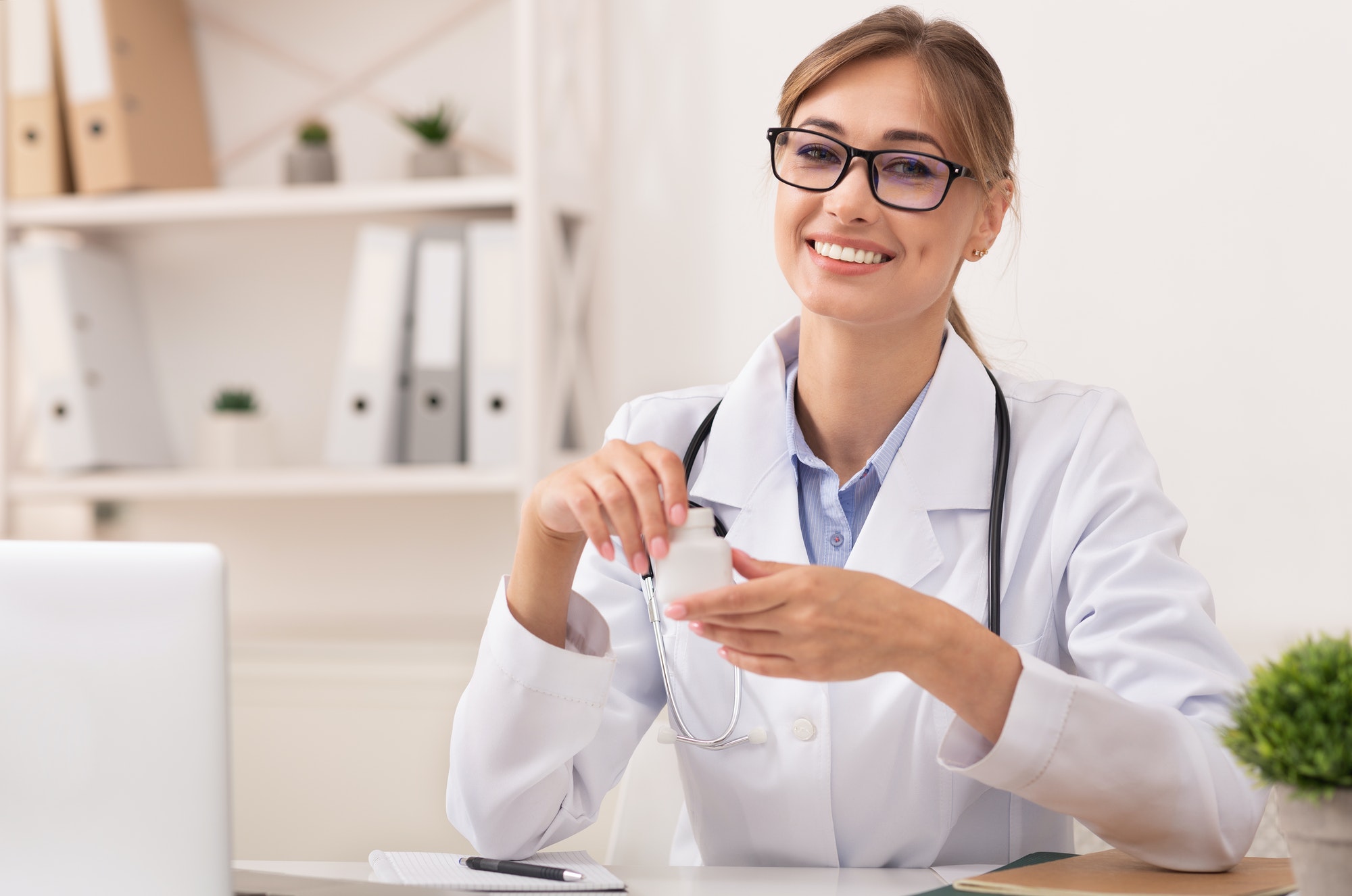Smiling Doctor Woman Holding Prescribed Medication Jar Sitting In Office
